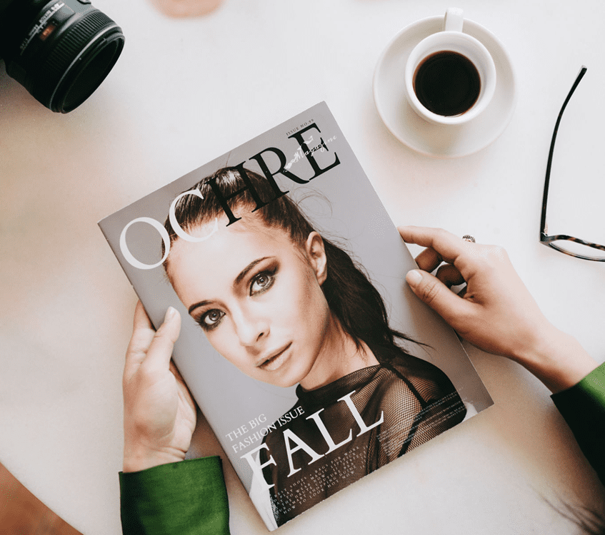 Magazine, camera, coffee, and glasses on table.