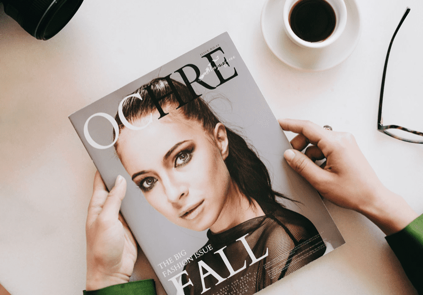 Magazine, camera, coffee, and glasses on table.